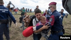 A migrant carrying a baby is stopped by Hungarian police officers as he tries to escape on a field nearby a collection point in the village of Roszke, Hungary, Sept. 8, 2015. (REUTERS/Marko Djurica)