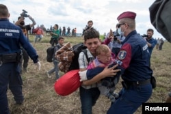 A migrant carrying a baby is stopped by Hungarian police officers as he tries to escape on a field nearby a collection point in the village of Roszke, Hungary, Sept. 8, 2015.