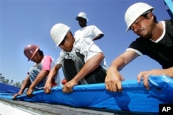 FILE - Immigrant workers, from left, Marcos Jamangape, Abel Tapia, Jack Horne, standing, and Joaquin Garcia install a plastic tarp as temporary protection Oct. 23, 2005, for a home damaged by Hurricane Katrina in Gulfport, Miss.
