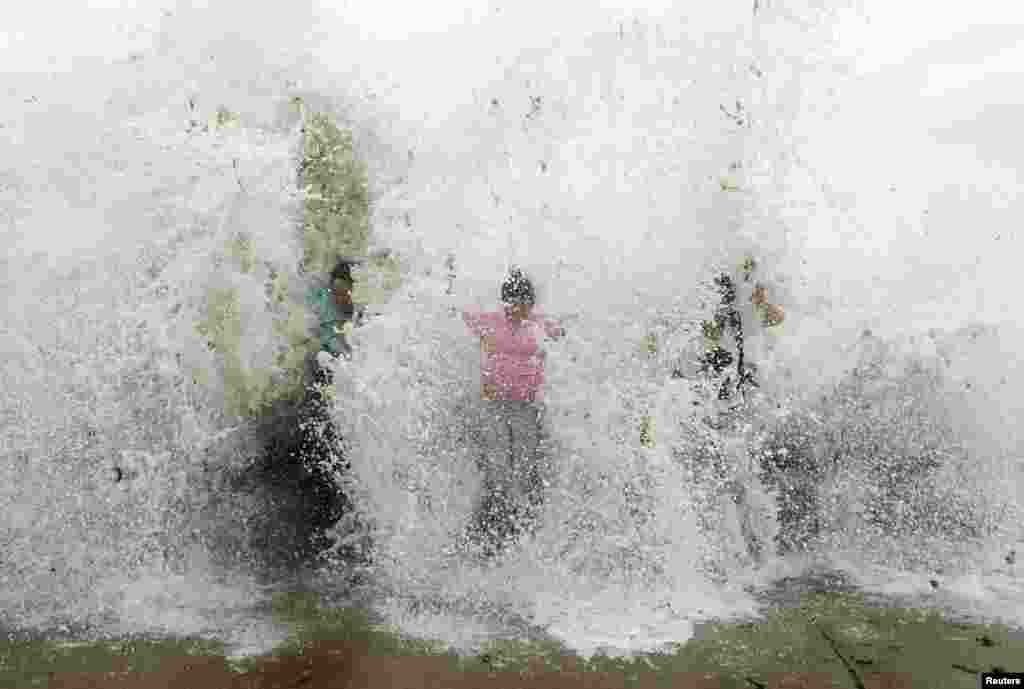 Tourists standing near the sea shore are hit by a wave, which surged past a barrier under the influence of Typhoon Chan-hom, in Qingdao, Shandong province, China.