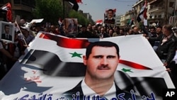 Pro-Syrian President Bashar Assad supporters hold Assad's poster with Arabic words reading: "I'll not kneel as long as you are my leader," as they demonstrate to show their support for their President, in Damascus, Syria.