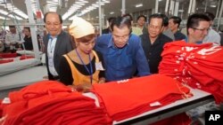 FILE PHOTO - Prime Minister Hun Sen, center, leans over a garment worker during a visit to a factory outside of Phnom Penh, Cambodia, Wednesday, Aug. 30, 2017. 