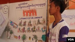 A member of the Community Youth Network stand near his artwork to raise awareness on safe migration​ at the annual reflection workshop on “Result and Role of CYN in Raising Awareness on Safe Migration and Prevention of Human Trafficking in Cambodia” on June 12, 2015, Phnom Penh. (Nov Povleakhena/VOA Khmer) 