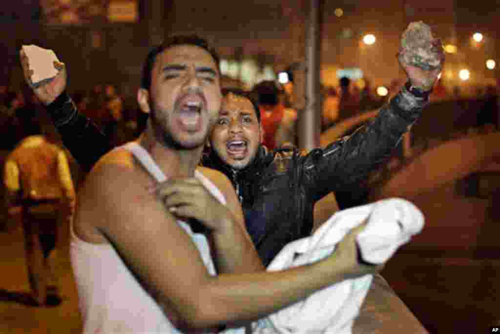 January 26: A protester, right, holds rocks in the air, ready to throw at riot police, as he urges other protesters on, during clashes in Cairo, Egypt, in the early morning. Egyptian police fired tear gas and rubber bullets and beat protesters to clear th