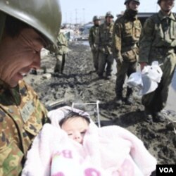 Tentara Jepang menggendong seorang bayi yang diselamatkan dari rumah keluarganya di Ishimaki City, Miyagi (14/3).