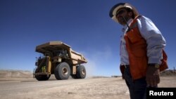 FILE - A worker checks Chile's Esperanza open pit copper mine as a truck travels along a road near Calama town, about 1,650 km (1,025 miles) north of Santiago, March 30, 2011. 