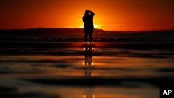 FILE - A woman photographs the sunrise at Ocean Park, in Old Orchard Beach, Maine, July 12, 2018.
