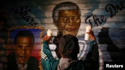 A man holds candles in front of a mural of former South African President Nelson Mandela and U.S. President Barack Obama in New York, Dec. 5, 2013.