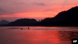 In this March 4, 2011, file photo, men ride in a boat across the Mekong River in Luang Prabang, Laos. It is officially described as the best-preserved city in Southeast Asia, a bygone seat of kings tucked into a remote river valley of Laos. Luang Prabang weaves a never-never land spell on many a visitor with its tapestry of French colonial villas and Buddhist temples draped in a languid atmosphere. (AP Photo/Jacquelyn Martin, File)