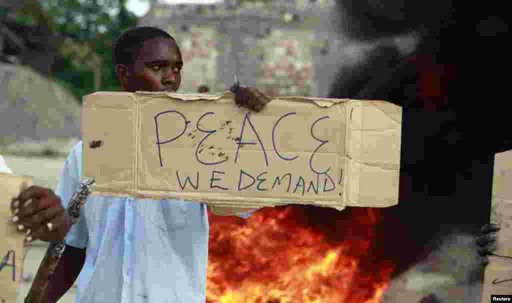 A resident holds a sign as he participates in a protest against the recent attack by gunmen in the coastal Kenyan town of Mpeketoni, June 17, 2014. 