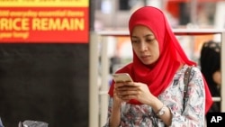 FILE - A Malaysian Muslim woman checks her mobile phone while shopping at a mall outside Kuala Lumpur, Malaysia, Aug. 18, 2015. 