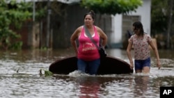A woman (L) and her daughter carry a table on a flooded street as they leave their home in San Miguel neighborhood in Asuncion, Paraguay. Dec. 27, 2015.
