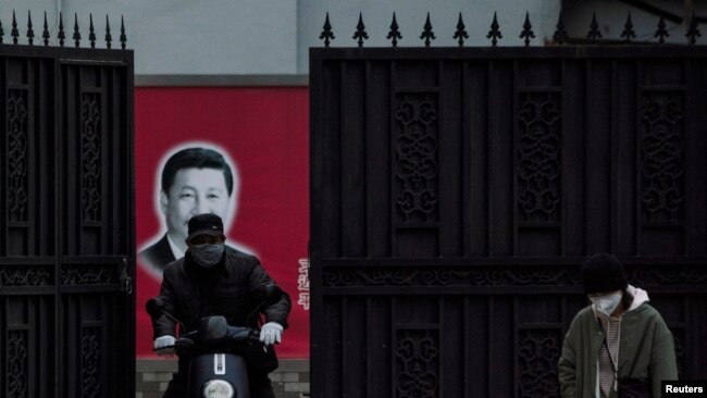 戴着口罩的行人从上海街头一个有着习近平画像的大门前经过。（2020年2月10日）