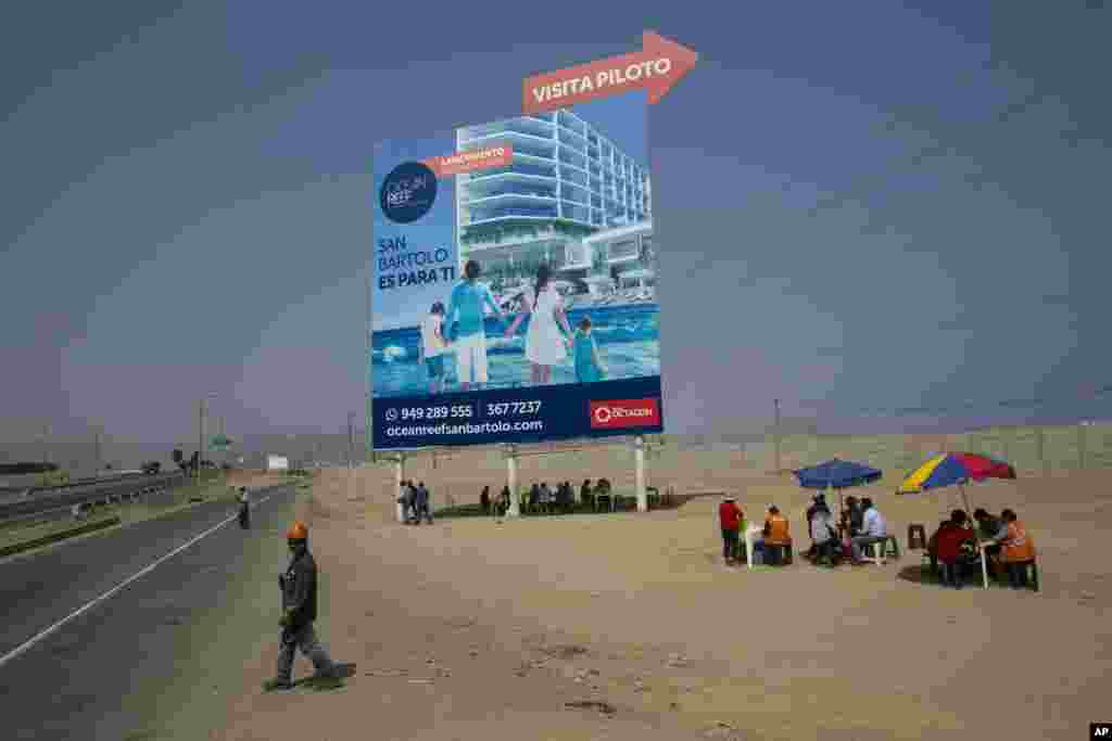 Workers eat lunch in the shade of a giant billboard advertising condos for sale, in a poor neighborhood on the south side of Lima, Peru.