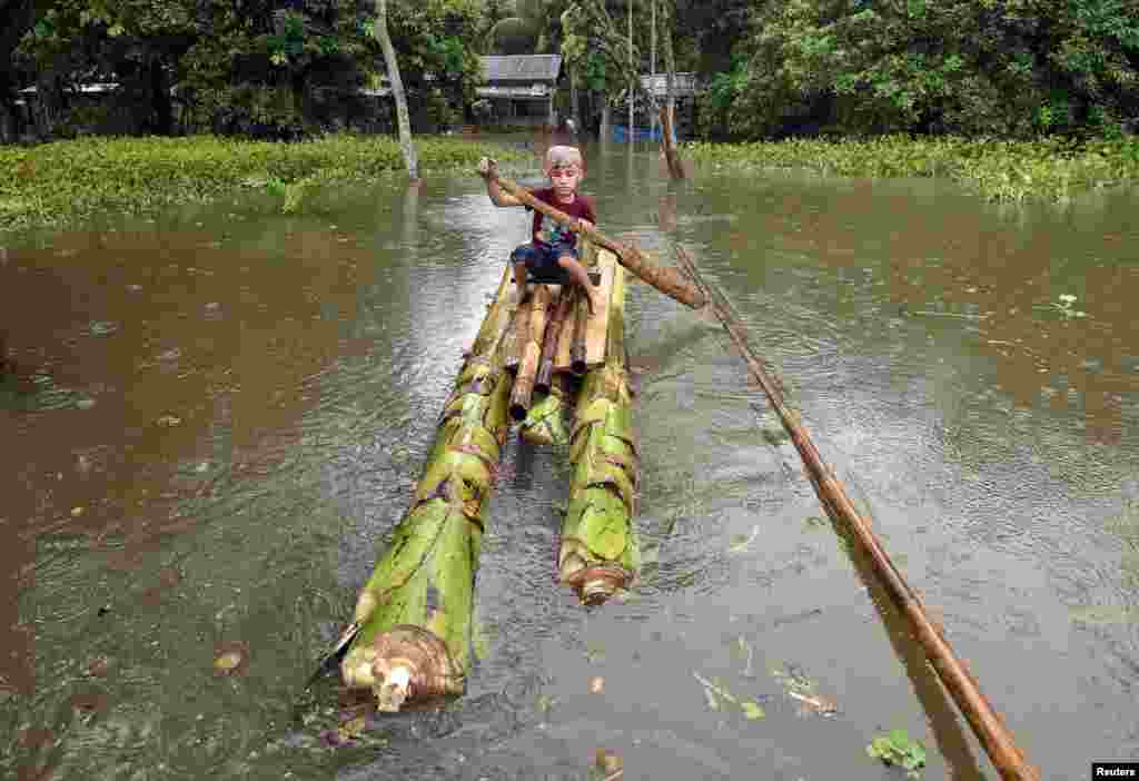 Seorang anak laki-laki menggunakan rakit buatan dari batang pohon pisang untuk menyeberangi desa Kuthori yang dilanda banjir di Nagaon, negara bagian Assam, India.