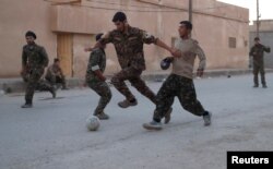 Kurdish fighters from the People's Protection Units (YPG) play football on a street in Raqqa, Syria, June 26, 2017.