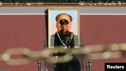 FILE - A paramilitary soldier stands guard behind a chain as the giant portrait of the late Chinese Chairman Mao Zedong is seen in the background in Tiananmen square, Nov. 12, 2013.