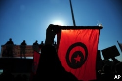 FILE - Tunisian police officers wave the national flag and posters as they demonstrate outside the presidential palace in Carthage near Tunis, Tunisia, to demand a pay increase, Jan. 25, 2016.