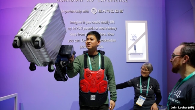 Eric Lynn lifts a 50 pound suitcase with the help of a powered arm similar to the Sarcos Robotics Guardian XO at the Delta Airlines booth during the CES tech show, Wednesday, Jan. 8, 2020, in Las Vegas.