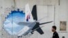 Seorang pelayan berjalan melewati mural penerbangan MH370 di Shah Alam di luar Kuala Lumpur, Malaysia. (Foto: AP)