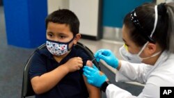 Eric Aviles, de 6 años, recibe la vacuna Pfizer COVID-19 de la farmacéutica Sylvia Uong en una clínica de vacunación pediátrica para niños de 5 a 11 años establecida en la Escuela Intermedia Willard en Santa Ana, California, el 9 de noviembre de 2021.