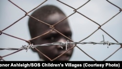 A young boy looks through the fence surrounding a safe place for children just outside Malakal. SOS Children's Villages says the children in its care need food and water, and aid agencies need more funds as food prices have spiked.