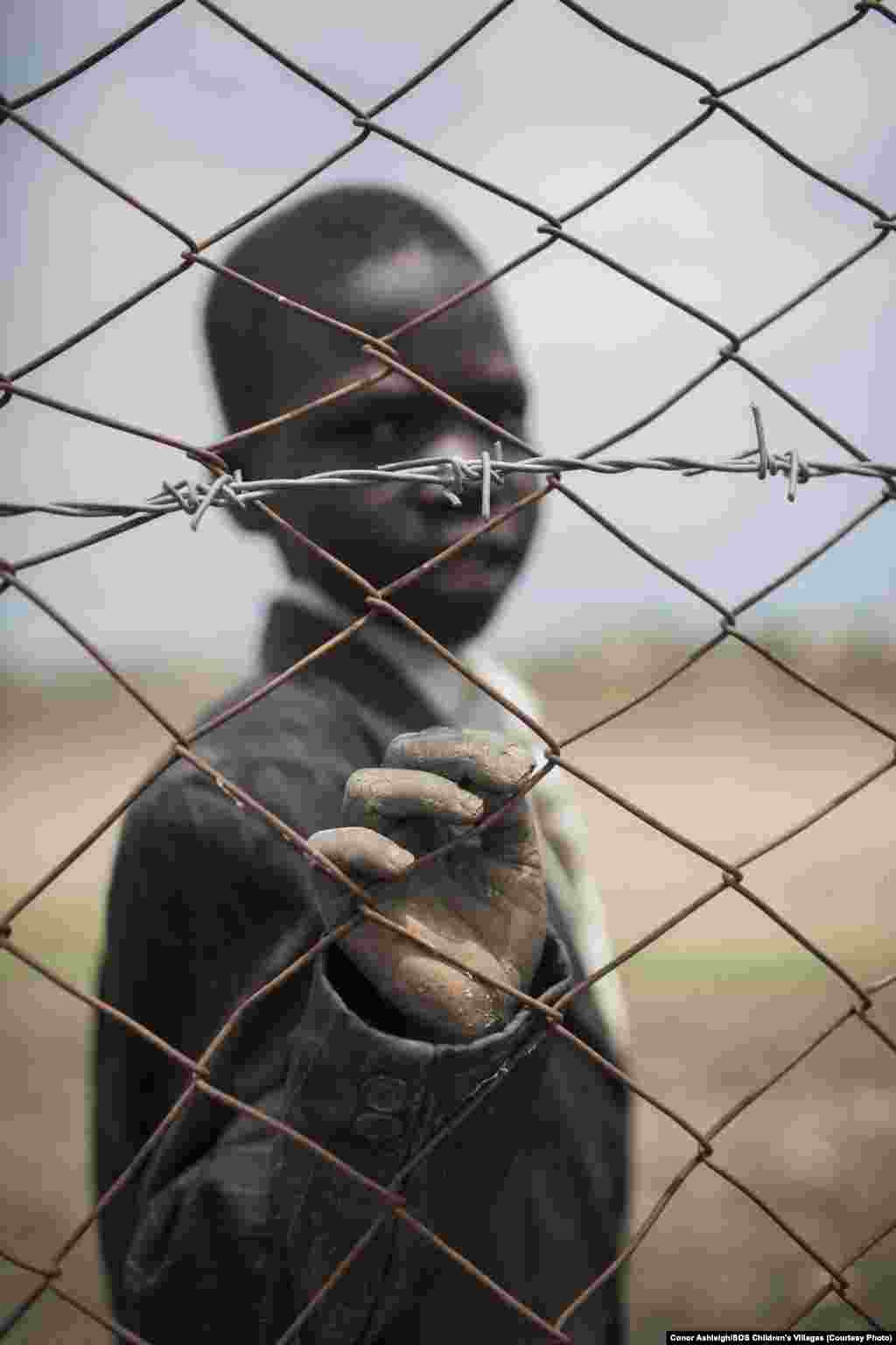 A young boy looks through the fence surrounding a safe place for children run by SOS Children&#39;s Villages, just outside Malakal in Upper Nile state. 