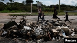 19일 브라질 북부 호라이마주의 국경 지역에서 베네수엘라 이주민들이 현지 주민들이 불태운 텐트 옆을 지나 이동하고 있다. 