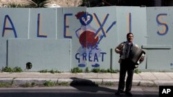 Atina'nın turistik Plaka semtinde "Büyük Alexis" yazılı duvar yazısının önünde akordeon çalan sokak çalgıcısı. Aleksis Çipras, kemer sıkma önlemlerinden bunalan Yunan halkının son umudu.