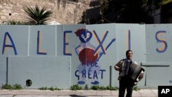 A busker plays music in front of a graffiti that refer to Greece's Prime Minister Alexis Tsipras in the traditional Plaka district of Athens, Feb. 21, 2015. 