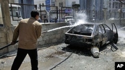 A Syrian municipality worker sprays water at a burnt car that was set on fire by Syrian anti-government protesters, in the southern city of Deraa, Syria, March 21, 2011