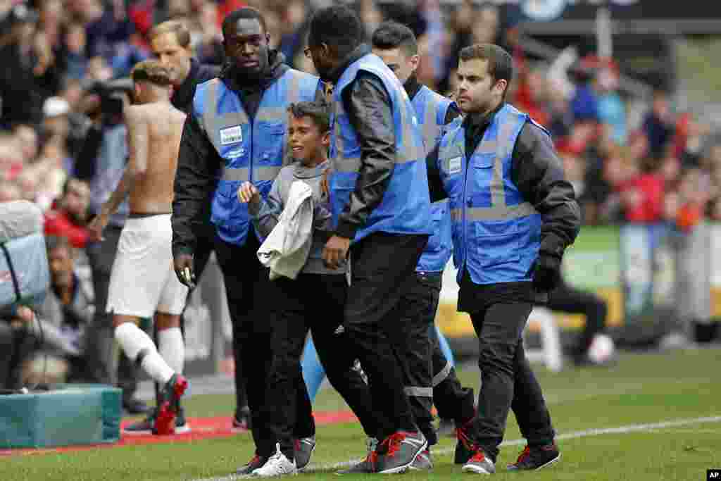 Security guards escort a crying boy who is holding the shirt PSG&#39;s Neymar, rear left, gave him after he ran onto the pitch at the end of the French League One soccer match between Rennes and Paris-Saint-Germain at Roazhon Park stadium in Rennes, western France.