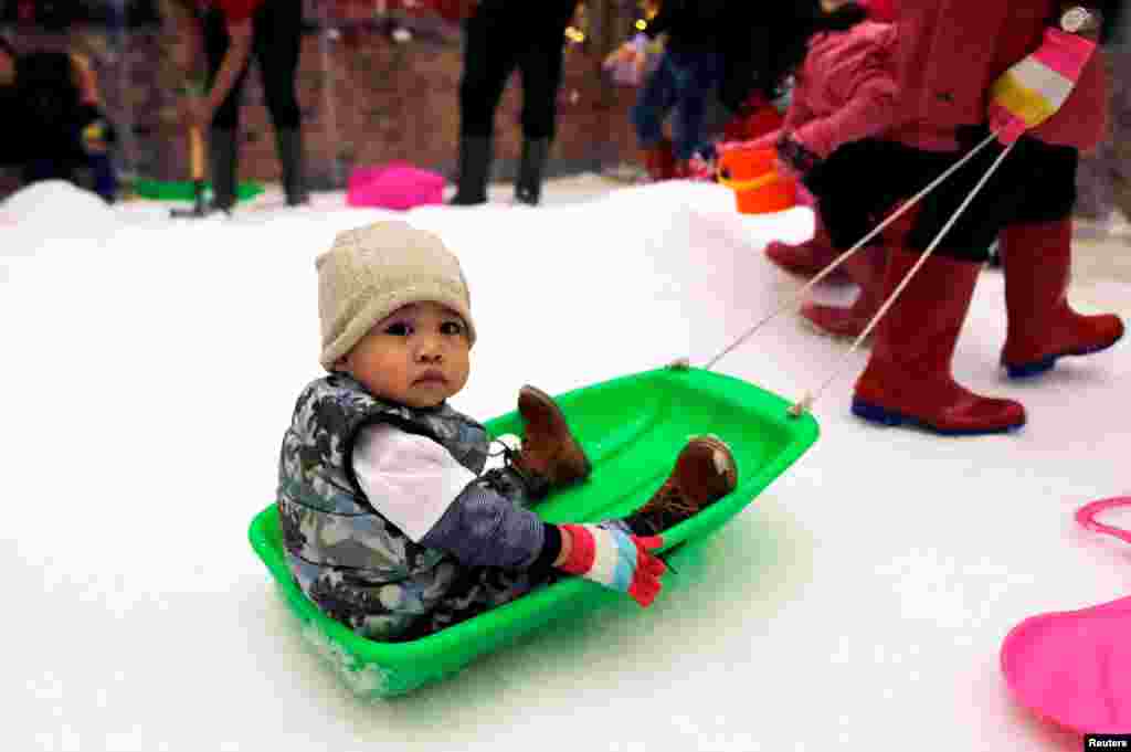 A child sits on a cart as children play with artificial snow during Christmas season at Lippo Mall Puri in Jakarta, Indonesia.