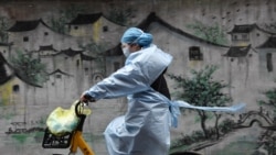 Una mujer circula en su bicicleta en Wuhan, vestida con traje protector y mascarillas para evitar contagios.