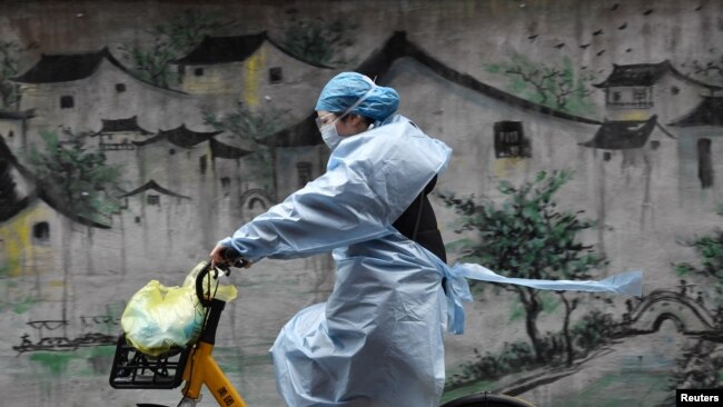 Una mujer circula en su bicicleta en Wuhan, vestida con traje protector y mascarillas para evitar contagios.