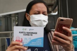 Seorang nakes memperlihatkan kartu vaksinasi setelah mendapatkan suntikan vaksin Covid-19 di sebuah puskesmas di Jakarta, Kamis, 14 Januari 2020. (Foto: Tatan Syuflana/AP)