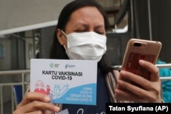 Seorang nakes memperlihatkan kartu vaksinasi setelah mendapatkan suntikan vaksin Covid-19 di sebuah puskesmas di Jakarta, Kamis, 14 Januari 2020. (Foto: Tatan Syuflana/AP)