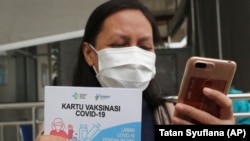 Seorang petugas medis memperlihatkan kartu vaksinasi setelah mendapatkan suntikan vaksin Covid-19 di sebuah puskesmas di Jakarta, Kamis, 14 Januari 2020. (Foto: Tatan Syuflana/AP)