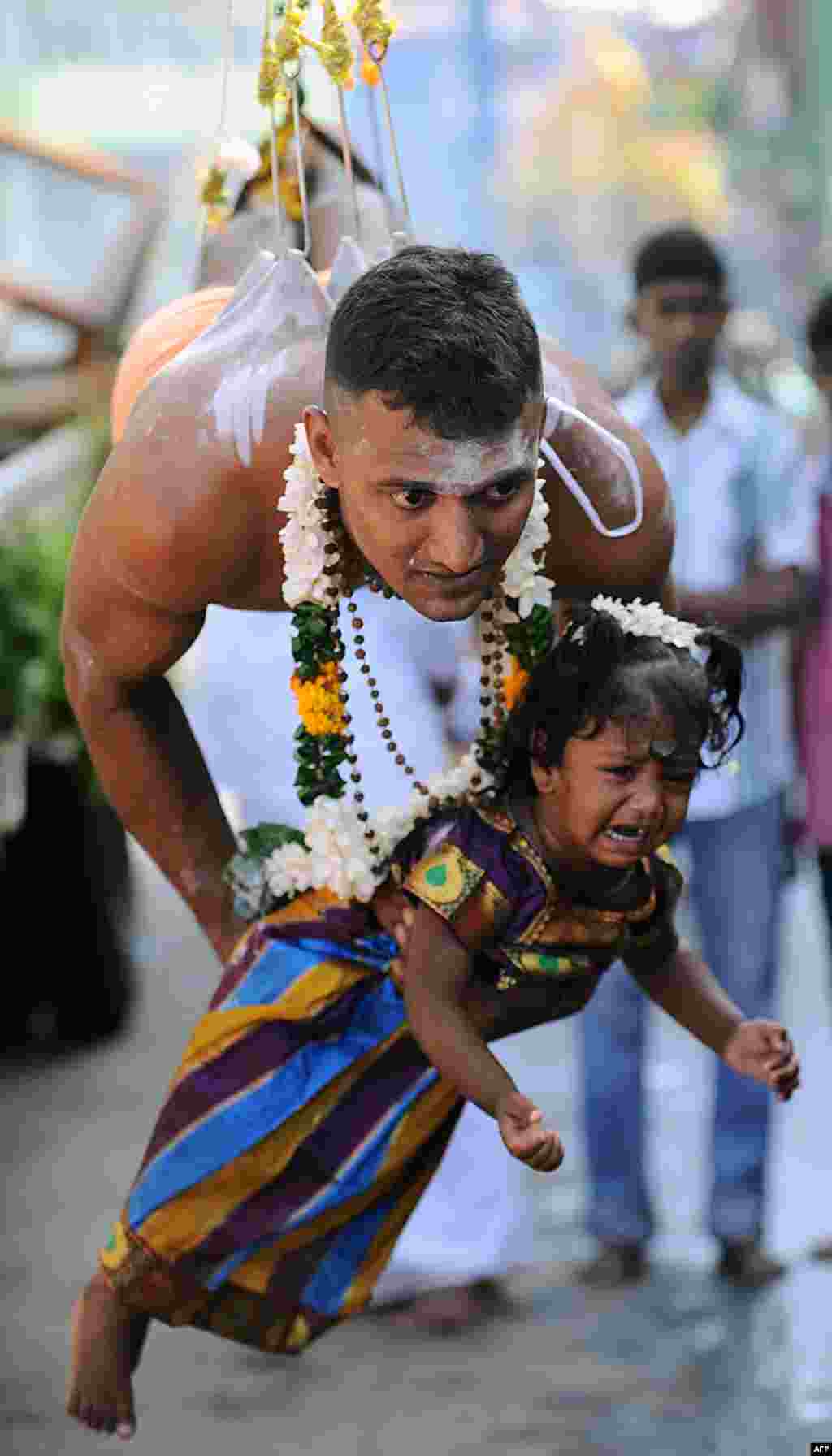 A Sri Lankan Tamil Hindu, suspended with hooks pierced through his body, carries a child while participating in the Vel Hinduism festival in Colombo.