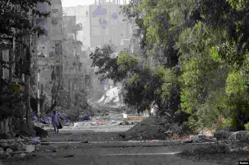 A man walks along a street filled with debris in Deir al-Zor, June 17, 2013. 