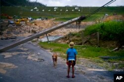FILE - In this Oct. 17, 2017 file photo, a boy accompanied by his dog watches the repairs of Guajataca Dam, which cracked during the passage of Hurricane Maria, in Quebradillas, Puerto Rico.