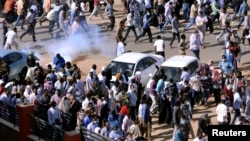 FILE - Demonstrators run from teargas lobbed to disperse them as they march along the street during anti-government protests in Khartoum, Sudan, Dec. 25, 2018. 