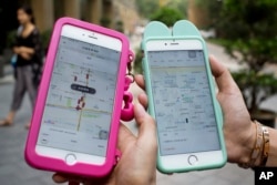 FILE - Women holding their smartphones show the ride-hailing apps Uber Technology Ltd., left, and Didi Chuxing at a residential compound in Beijing on Aug. 1, 2016.