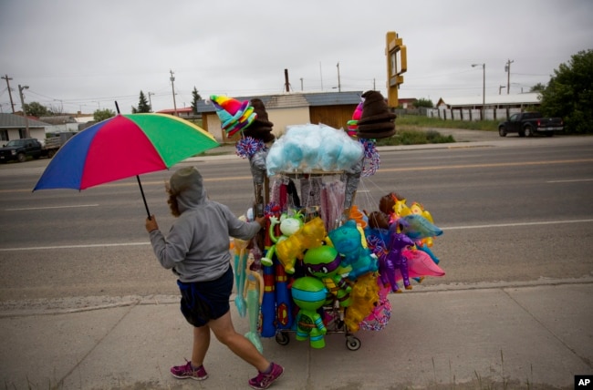 A vendor wheels her cart of souvenirs before the start of the North American Indian Days parade on the Blackfeet Indian Reservation in Browning, Mont., Saturday, July 14, 2018