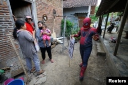 Agus Widanarko, 40, mengenakan kostum Spiderman sambil membawa spanduk saat menghibur anak-anak yang terkurung di rumah akibat pembatasan COVID-19, di Sukoharjo, Jawa Tengah, 10 September 2021. (Foto: Reuters)