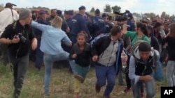 In this image taken from TV, a Hungarian camerawoman identified as Petra Laszlo, center left in blue, kicks out at a young migrant who had just crossed the border from Serbia near Roszke, Hungary, Sept. 8, 2015. 