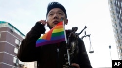 Yang Teng holds a statue depicting a goddess of justice and a flag symbolizing gay pride as he arrives at court in Beijing, Dec. 19, 2014.