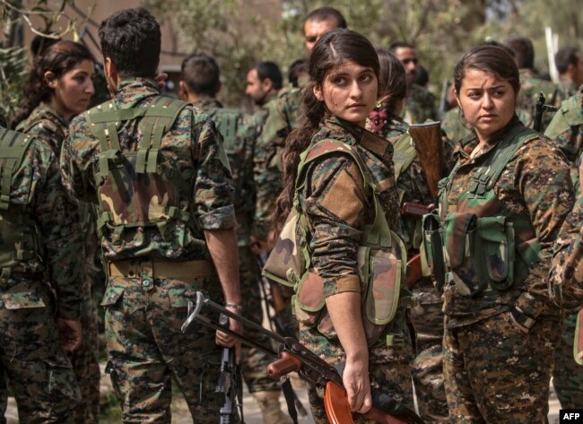 Fighters of the U.S.-backed Kurdish-led Syrian Democratic Forces (SDF), including women, gather to celebrate near the Omar oil field in the eastern Syrian Deir Ezzor province, March 23, 2019, after announcing the total elimination of the Islamic State's self-declared caliphate.