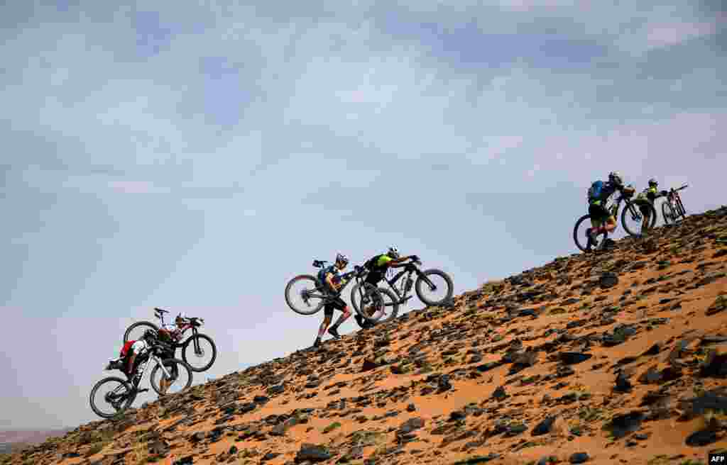 Competitors carry their bicycles along a sand dune during Stage 2 of the 14th edition of Titan Desert 2019 mountain biking race between Merzouga and Ouzina, Morocco.