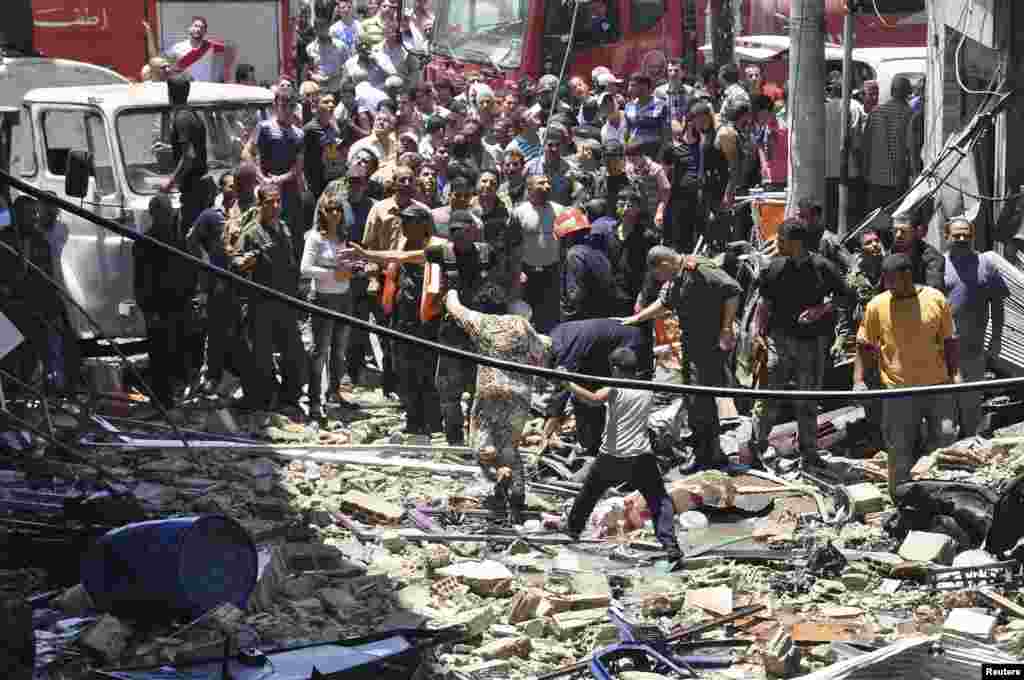 People gather around wreckage after a car bomb at the Wadi al-Dahab area of Homs in this picture released by Syria&#39;s national news agency SANA. The car bomb killed seven people and more than 55 were wounded, state media said.